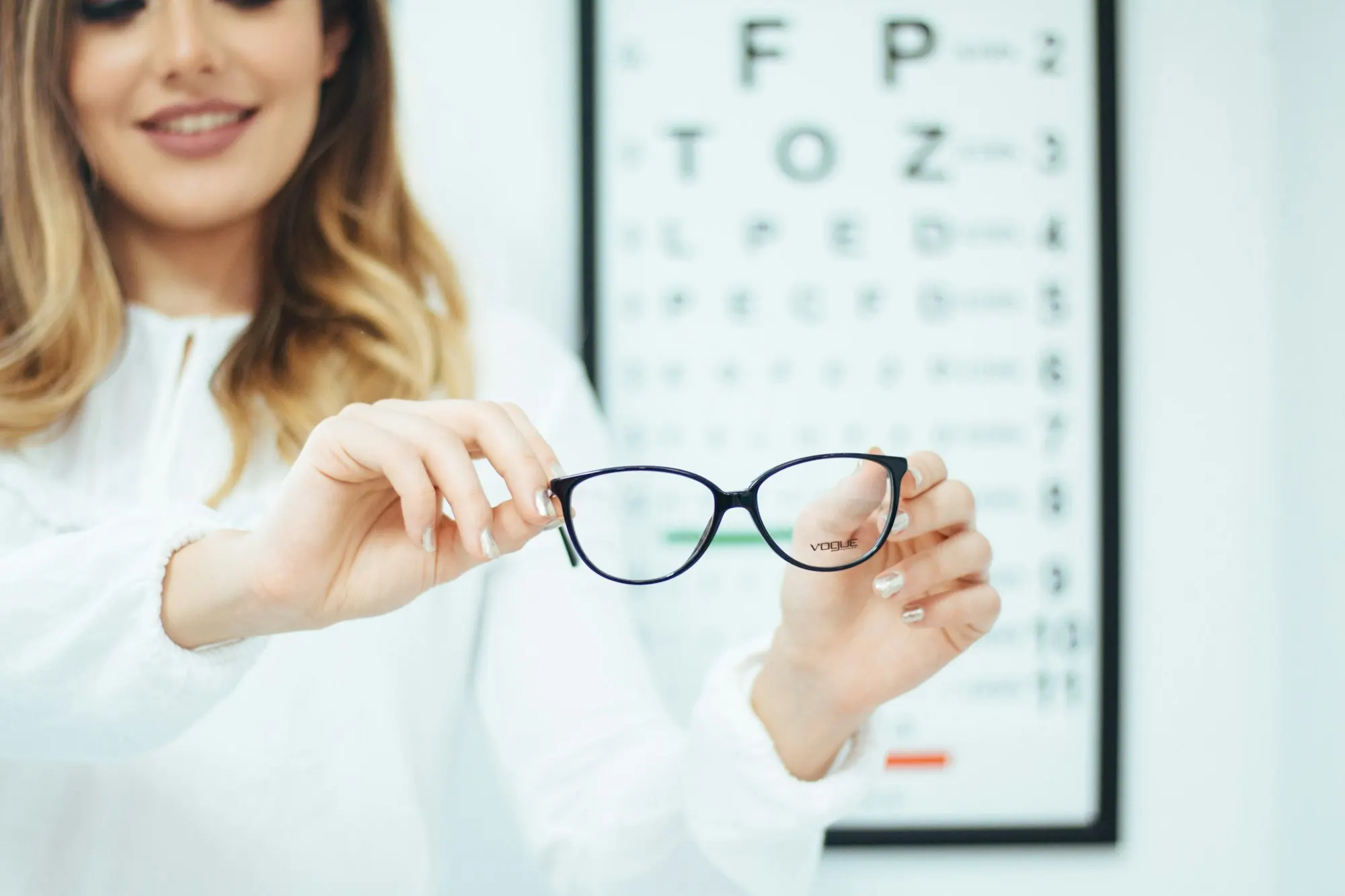 Optometrista sosteniendo unos lentes frente a una cartilla de agudeza visual