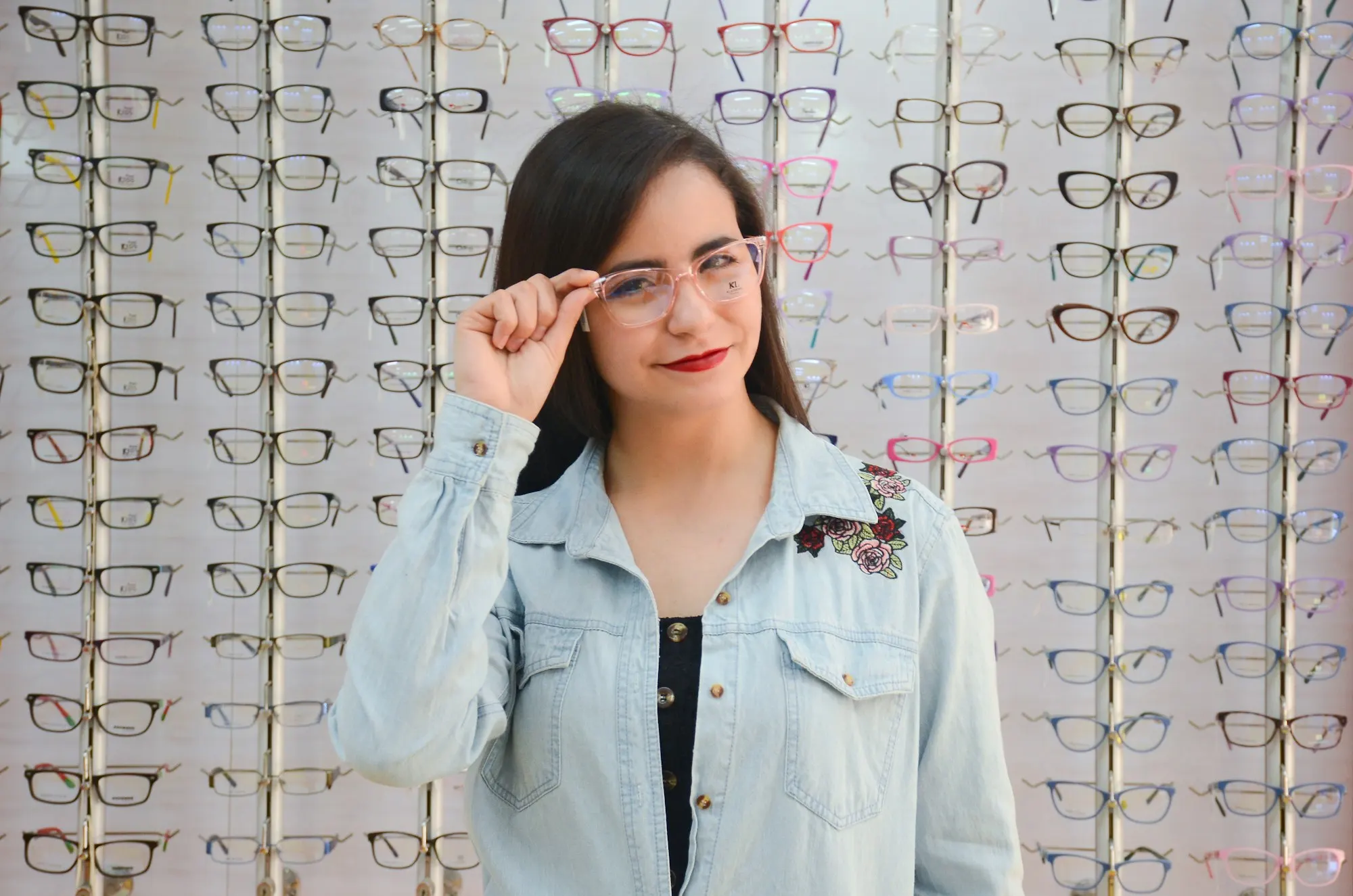 Mujer probándose armazones frente a una pared de lentes